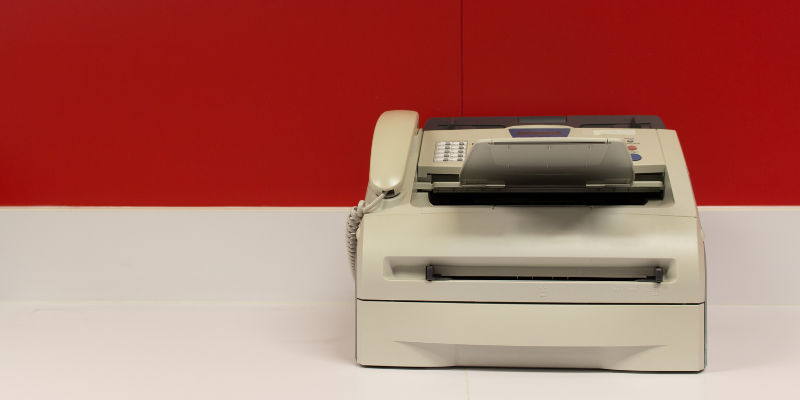 Fax machine on white table in front of red wall for a blogpost on how the referral process has evolved in the digital age.