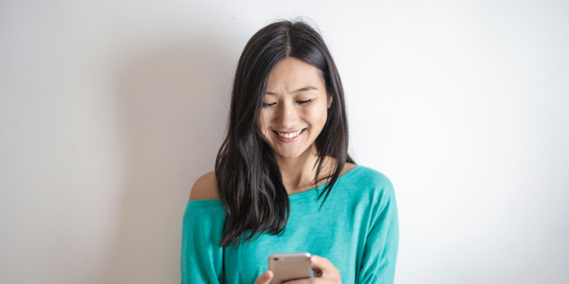 Woman looking at her phone and smiling standing in front of a white wall for a paragraph on how to make the referral capture process easier.