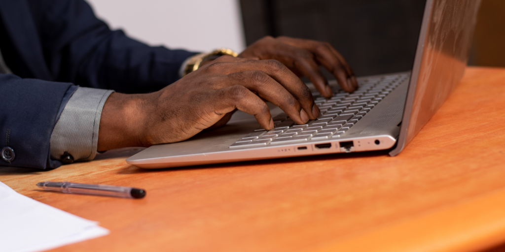 Male hands typing on a laptop sitting on a wooden table for a blogpost about the future of referral capture. 