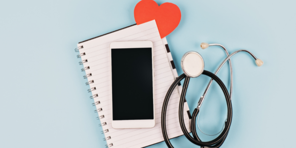 A phone, notebook, stethoscope and heart on a table to reflect all that goes into communication with patients.