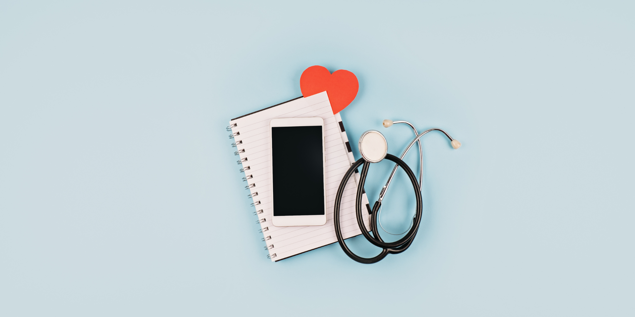 A phone, notebook, stethoscope and heart on a table to reflect all that goes into communication with patients.